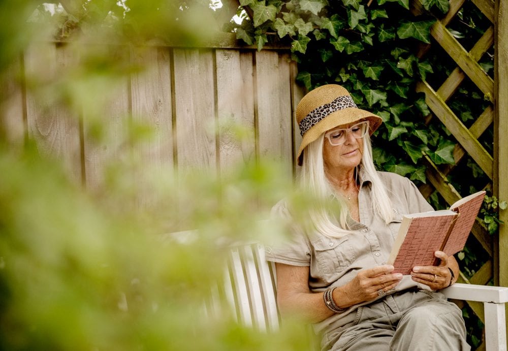 Ældre kvinde læser i bog på terrassen
