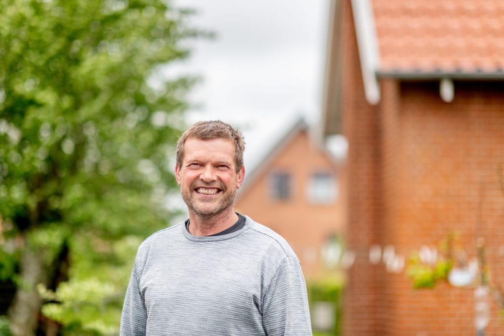 en mand står i en have foran et rødt hus