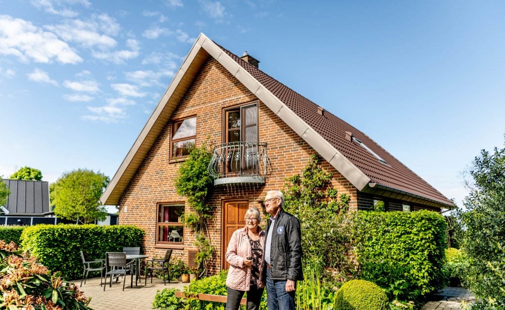 en mand og en dame står foran et hus i en have